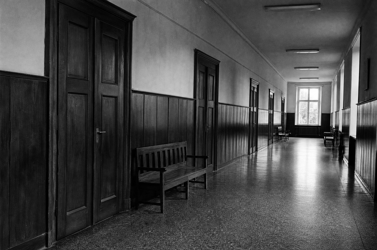 Długi korytarz w budynku sądu z drewnianymi drzwiami, boazerią i ławką pod ścianą