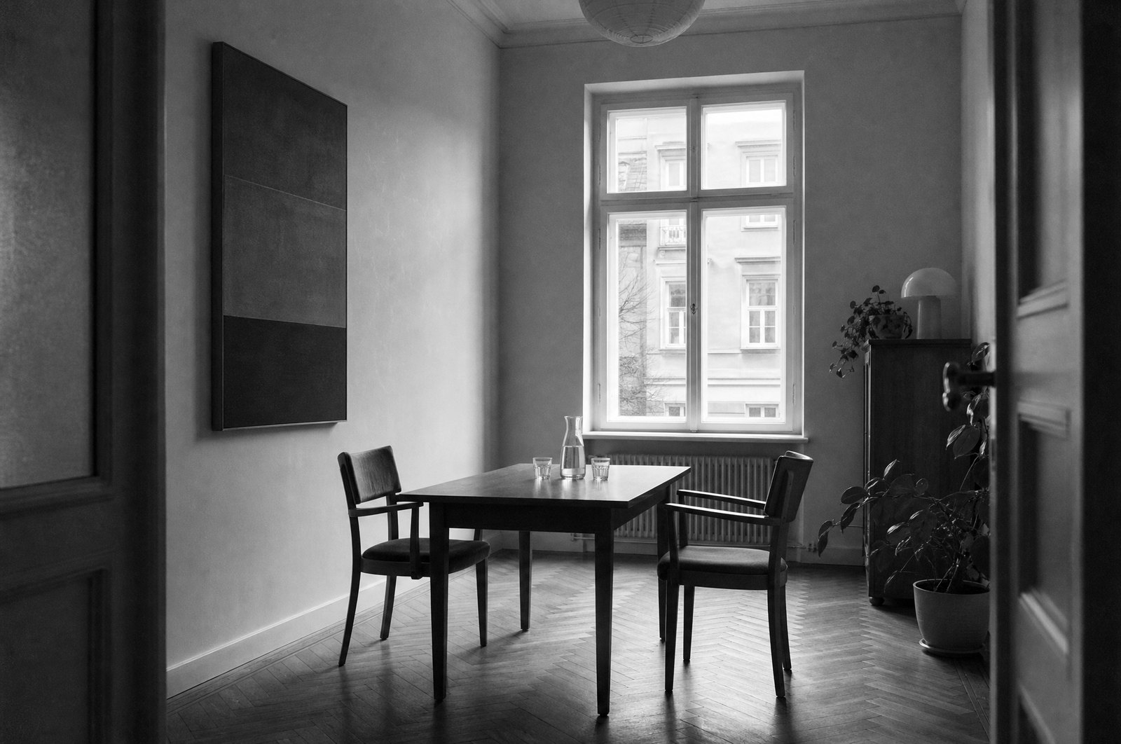 Pusta sala spotkań w kamienicy: stół z krzesłami, karafka i szklanki, wysokie okno